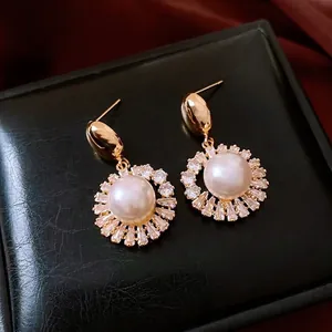 Elegant gold-plated pearl flower earrings with zircons on a black leather background