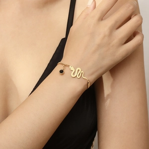 Close-up of gold snake chain bracelet with black stone pendant worn on a model's wrist