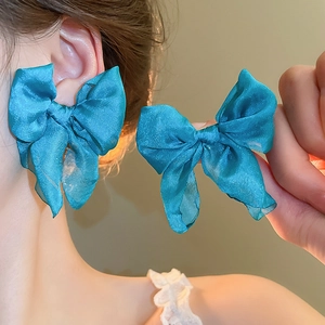 Detail of teal chiffon bow earrings featuring layered fabric and silver needle design