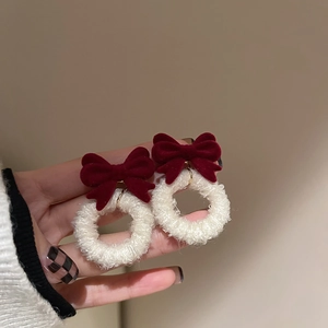 Close-up of red flocked bow earrings with plush white rings for winter festive style