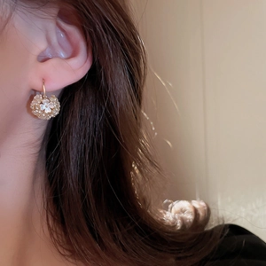 Close-up of floral ball earring featuring white acrylic flowers with gold plating on model