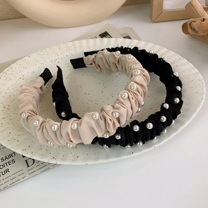 Eleganti cerchietti in tessuto plissettato beige e nero con perle su un vassoio ceramico