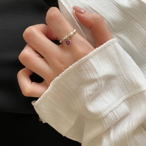 Detail of twisted 925 silver ring with a dangling magenta heart pendant on model's finger