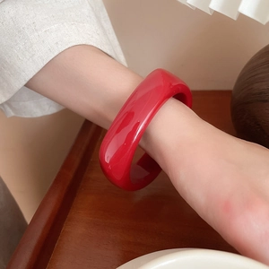 Detailed view of a bold glossy red resin bangle bracelet worn on a wrist in warm lighting
