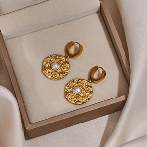 Irregular golden hammered metal earrings with central pearl in a beige velvet jewelry box
