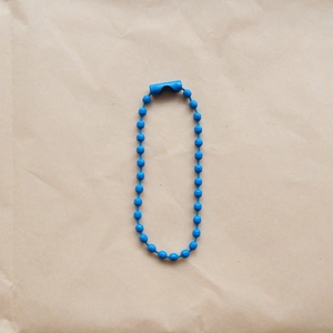 Detailed view of a 2.4mm blue coated metal bead chain with connector on craft paper