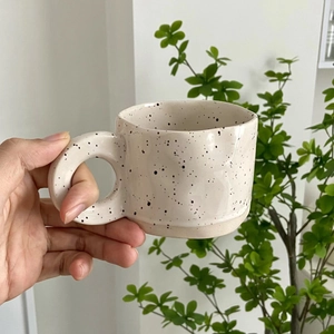 Close-up of hand holding a speckled ceramic coffee mug with large round handle and ink splash