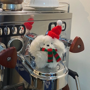 Close-up of white plush toy wearing a festive Christmas hat on a chrome espresso machine