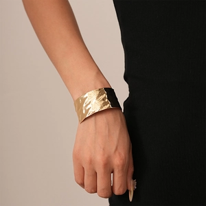 Detailed view of wide gold cuff bracelet with irregular hammered texture on model
