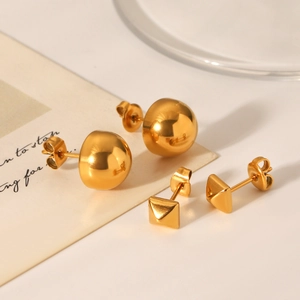 Close-up of geometric gold-plated stud earrings featuring sphere and pyramid designs