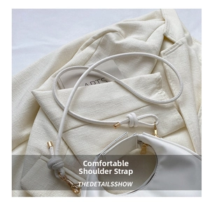 Detail view of smooth white leather bag featuring knot design and golden hardware zipper