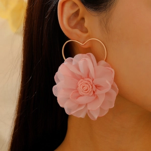 Dettaglio di orecchini a fiore in tessuto rosa con cornice a cuore dorata su modella