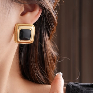 Close-up of vintage square golden earrings with black enamel inlay on a female model