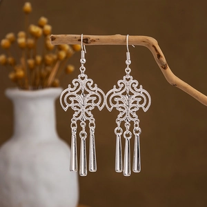 Macro detail of silver ethnic earrings featuring hollow leaf patterns and tassel bells