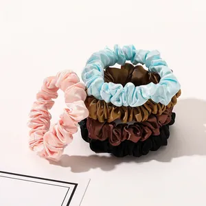 Detail view of five satin silk scrunchies in pink, blue, gold, brown, and black colors