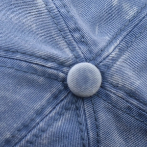 Close-up of the top button and stitching on a washed blue denim baseball cap detail