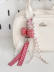 Detail van rood-witte geruite strik sleutelhanger met zilveren hart aan de tas