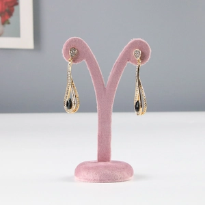 Detailed view of elegant gold drop earrings with black stones on pink velvet display stand