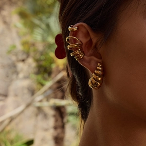 Detailed view of gold spiral earring and ear cuffs set worn on a model's ear