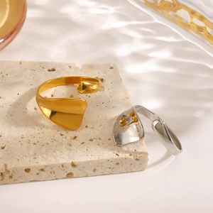 Polished liquid-style stainless steel rings in gold and silver on travertine stone