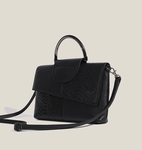 Detail of black faux crocodile and lychee leather handbag with metallic top handle