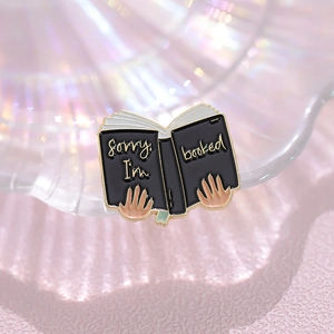 Detail of a black enamel book brooch with Sorry I'm booked text on iridescent background