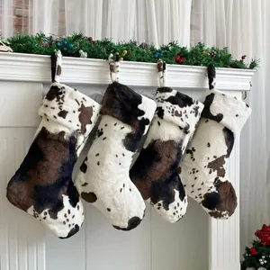 Set of four plush cow print Christmas stockings hanging on a white festive fireplace mantle