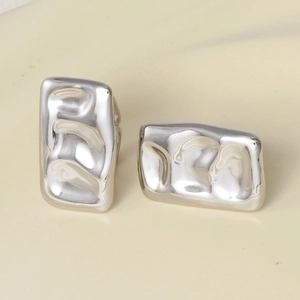Close-up of silver-tone rectangular earrings with irregular textured surface finish
