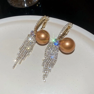 Close-up of golden pearl tassel earrings with shimmering rhinestones on a white plate