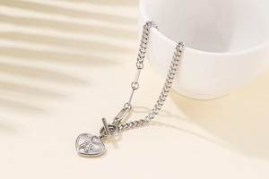 Detail of silver heart charm bracelet with T-bar clasp draped on white ceramic cup