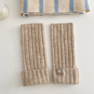 Detail of beige wool-blend knit arm warmers with vertical ribs and leather compass tag