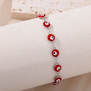 Detailed close-up of a silver chain bracelet with vibrant red Evil Eye enamel charms