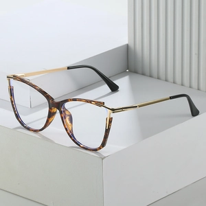Detail of tortoise shell cat-eye glasses frame with metallic gold accents on white pedestals