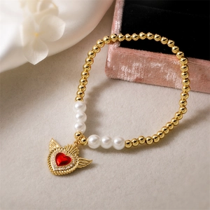 Detailed close-up of gold beads and pearl bracelet with a red winged heart pendant