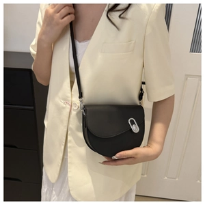 Detail of a black saddle bag with silver oval buckle styled with a white blazer