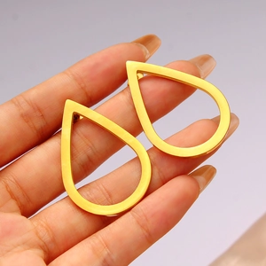 Polished gold hollow teardrop earrings held by hand to show size and geometric style