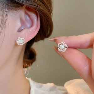 Detailed view of silver hollow flower stud earrings worn by a model in soft lighting