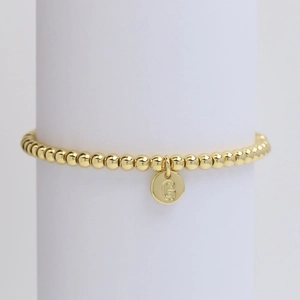 Detailed close-up of a gold-plated beaded bracelet featuring a round letter G pendant charm