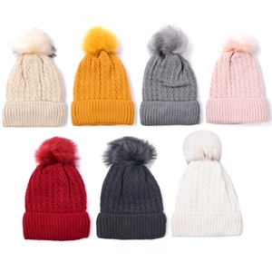 Variety of cable-knit beanies with pom-poms in seven assorted colors on a white background
