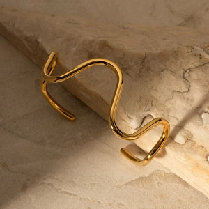 Macro shot of 18k gold plated wave-shaped necklace resting on a natural stone background