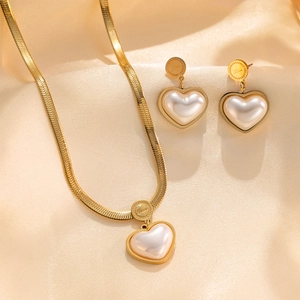 Elegant gold heart pearl necklace and earrings set displayed on champagne silk fabric
