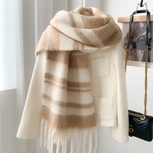 Detailed view of soft beige and camel striped scarf with tassel fringe on white coat