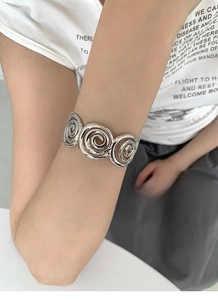 Close-up of a silver geometric spiral open bangle worn on a wrist with a casual outfit
