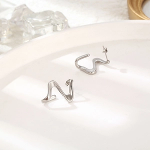Abstract geometric silver titanium earrings with wavy lines on a minimalist ceramic plate