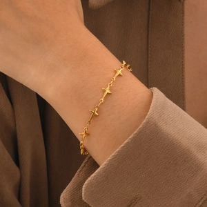 Elegant gold stainless steel bracelet with star charms on a woman's wrist with warm tones
