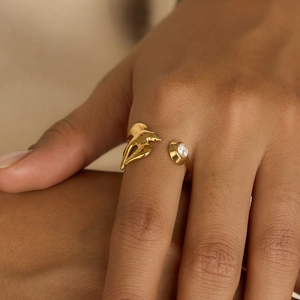 Detailed close-up of 18K gold olive leaf bird ring with white zircon on finger