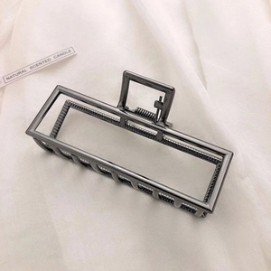 Macro view of gunmetal grey rectangular metal hair claw clip on white silk fabric
