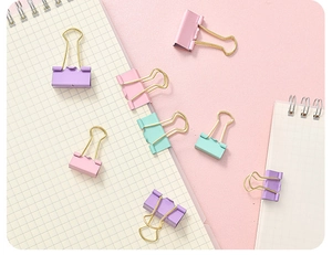 Close-up of hollow metal binder clips in macaron colors over a grid notebook