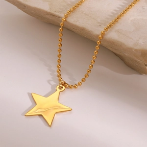 Detail of a polished gold star pendant on a beaded chain over a natural stone
