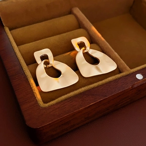 Macro detail of golden irregular geometric earrings with textured matte finish in a box